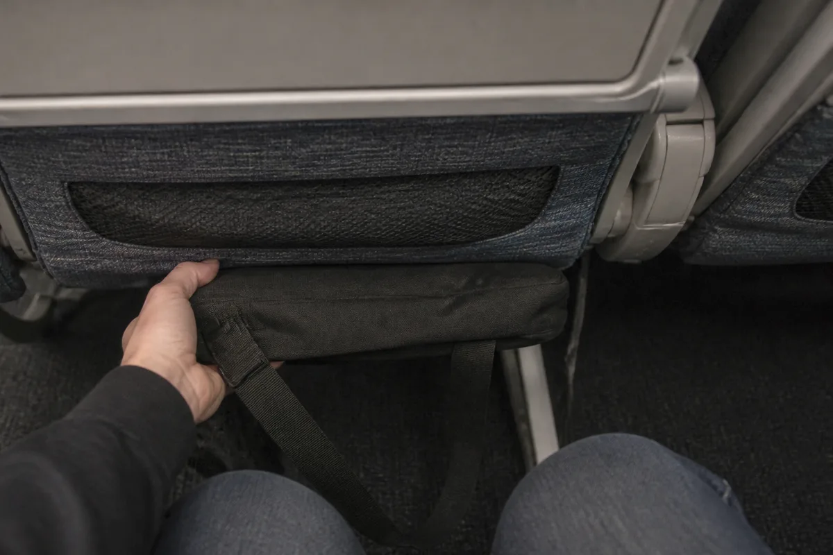 飛行機の前の座席の下にバッグを収納しているイメージ