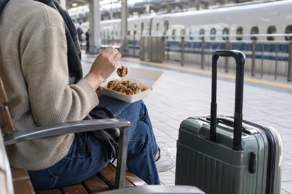 新大阪駅の新幹線ホームでたこ焼きを食べる乗り換え客のイメージ